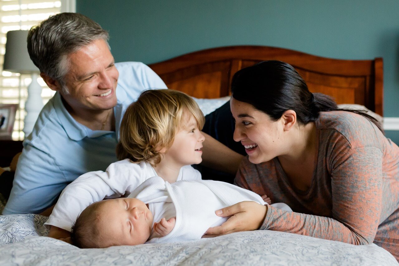 Dad and mom on bed woth toddler and baby.