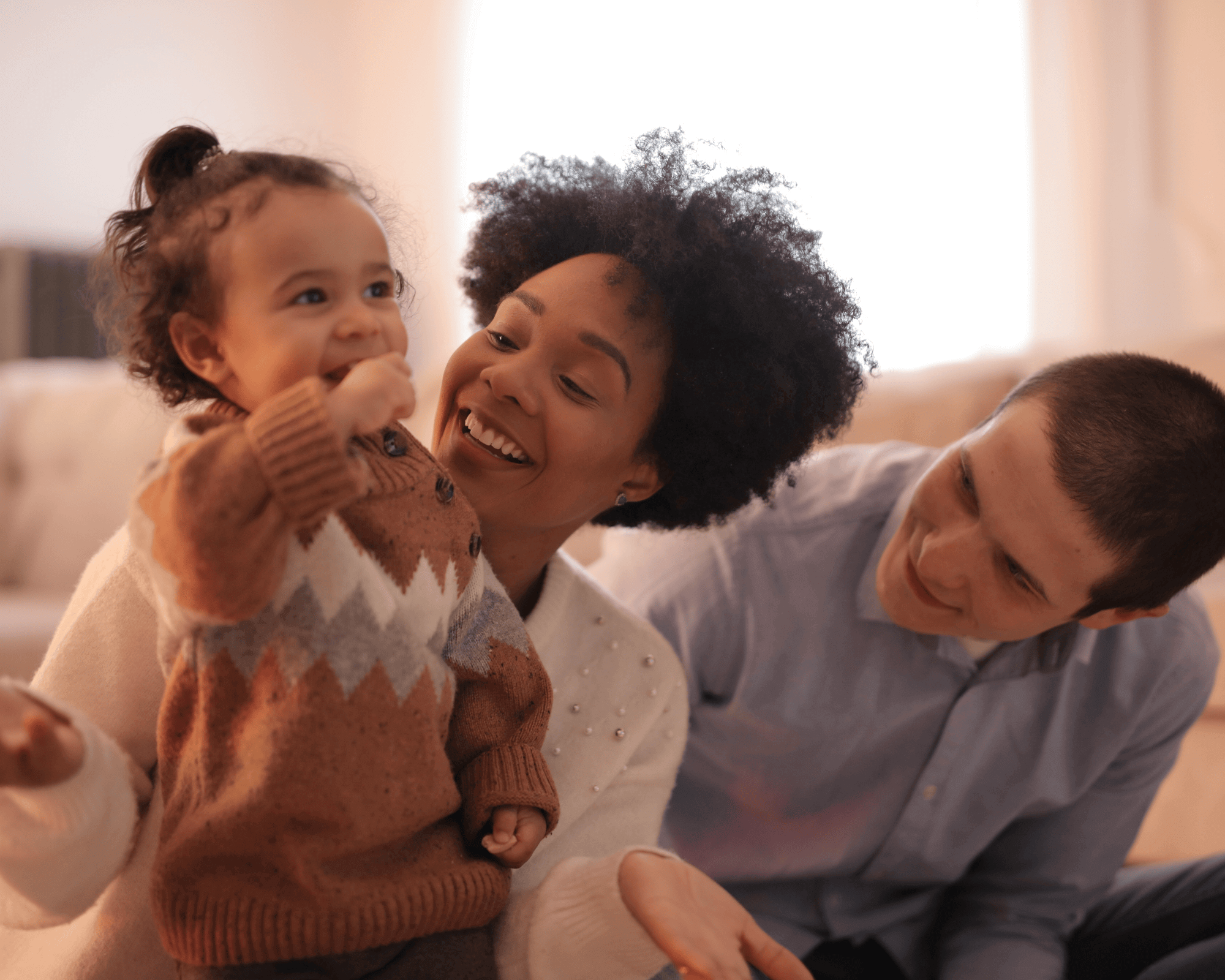 Mom and dad on couch smiling at little girl.