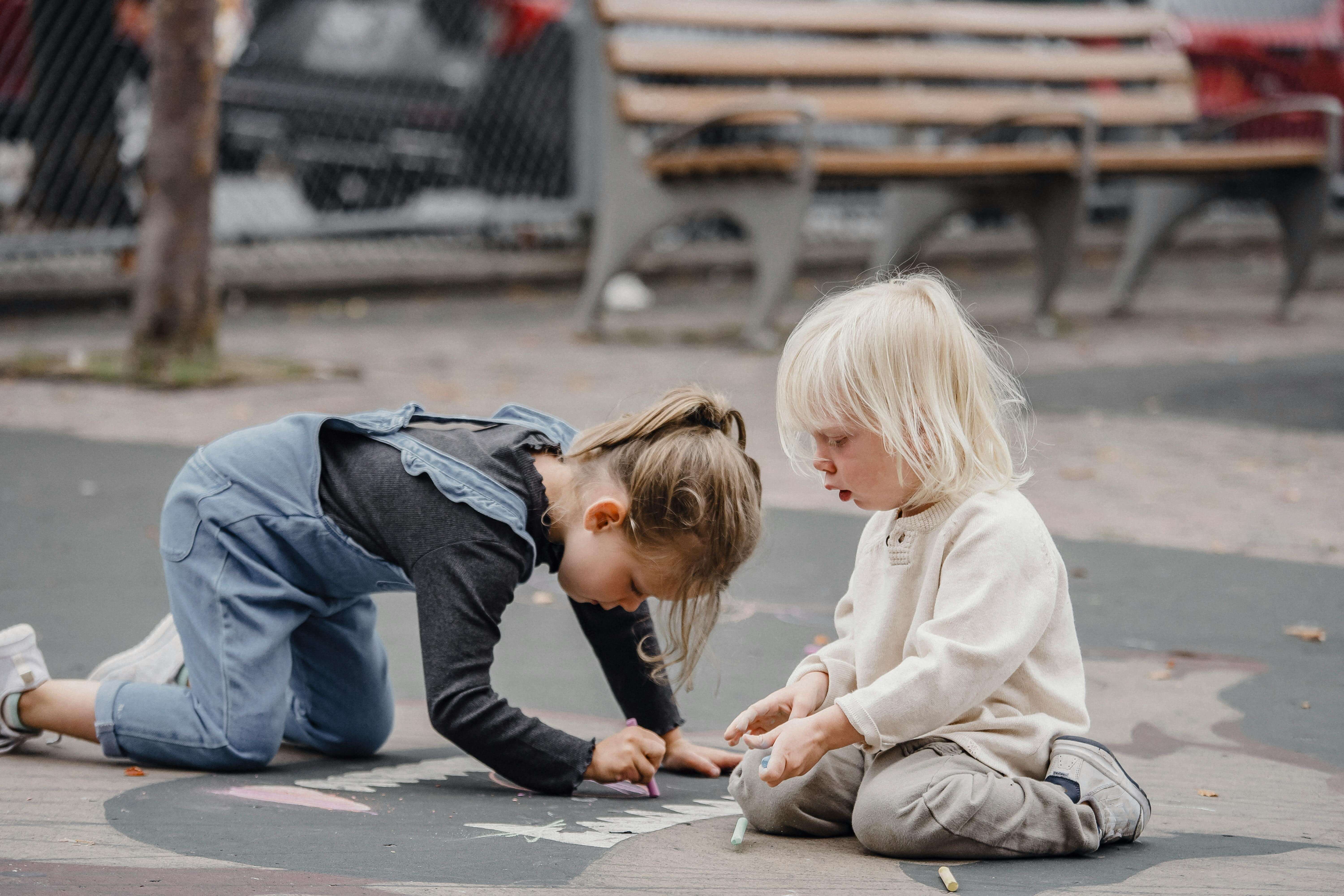 A couple of preschoolers drawing on the sidewalk.