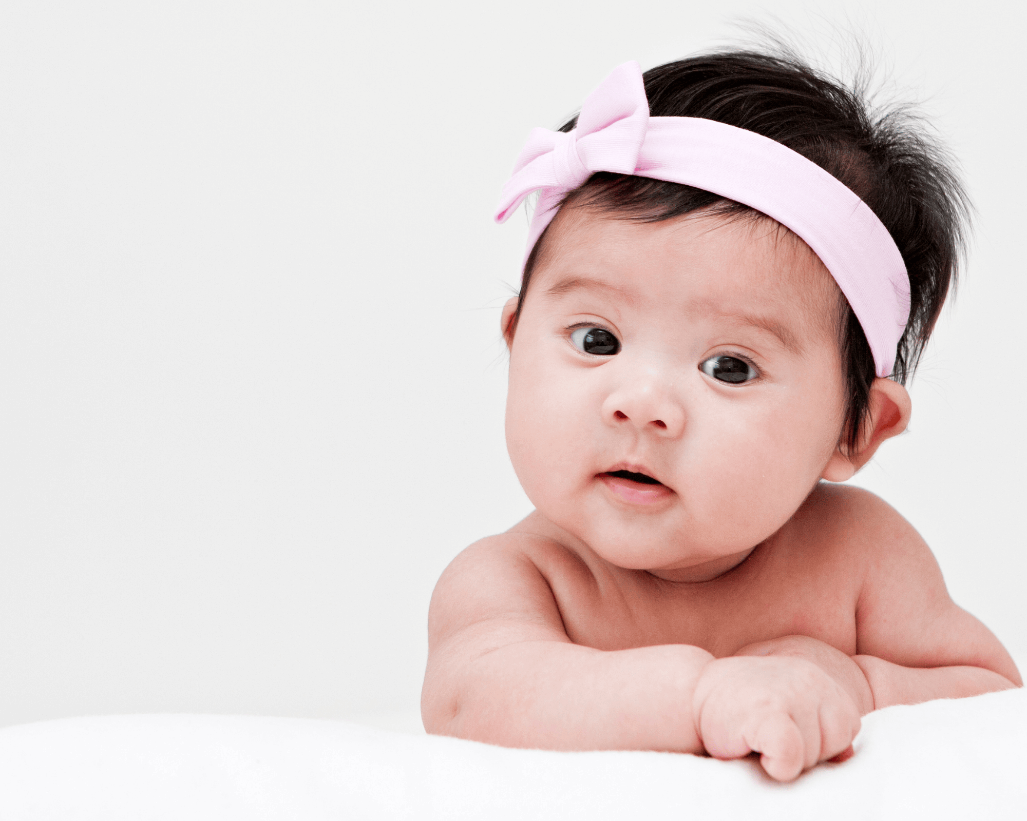 Baby girl sitting behind white blankey looking towards camera.