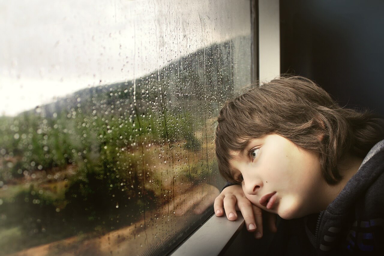 Child waiting at window with head on sill.